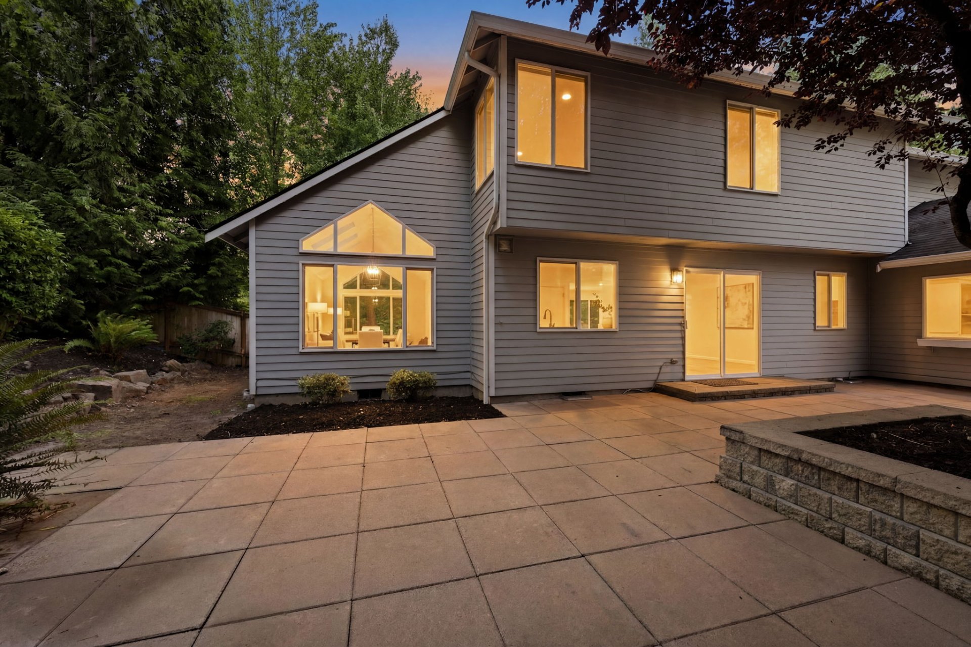 Fully fenced backyard with expansive paver patio at dusk